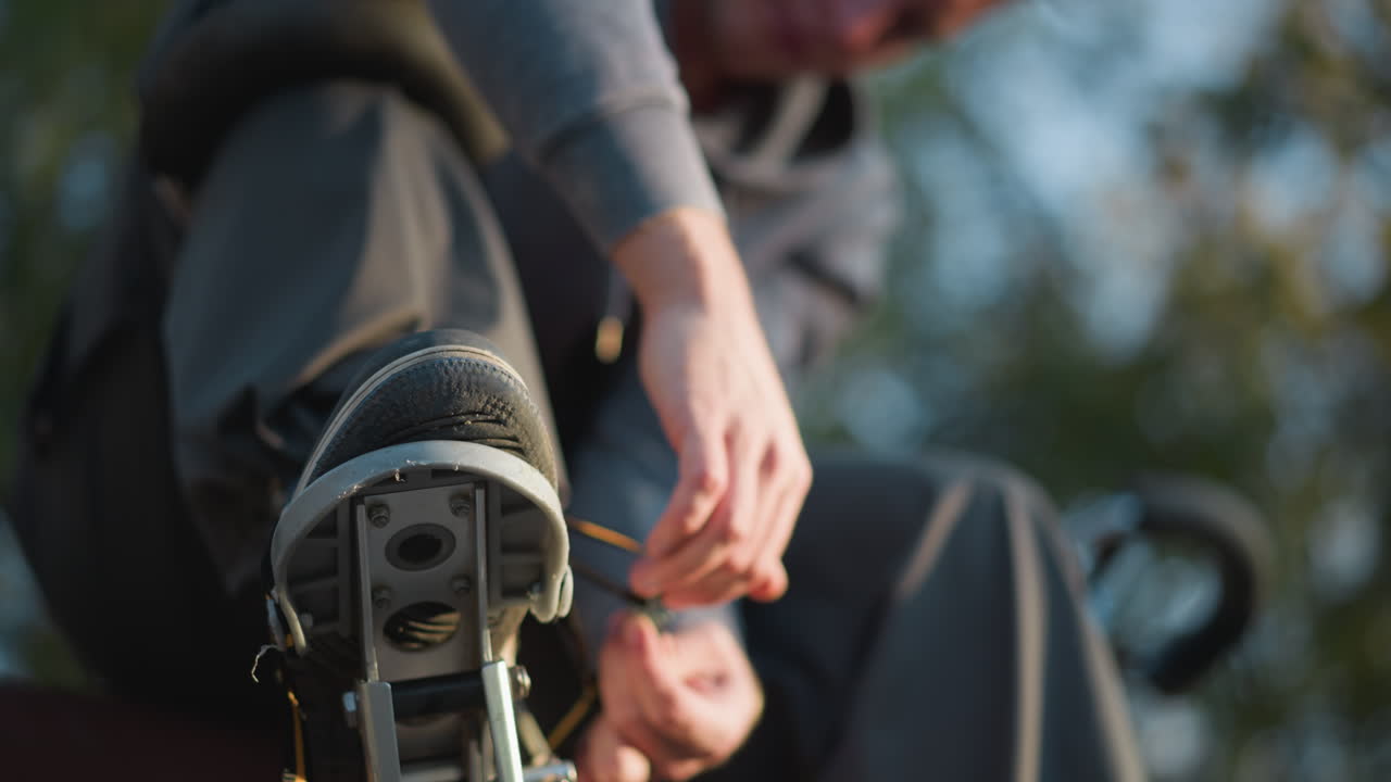 primer plano de la mano atando el zócalo al aire libre, persona con capucha gris, fondo borroso, enfoque en el proceso de ajuste, mostrando la precisión de la actividad y la configuración del equipo de zócalo