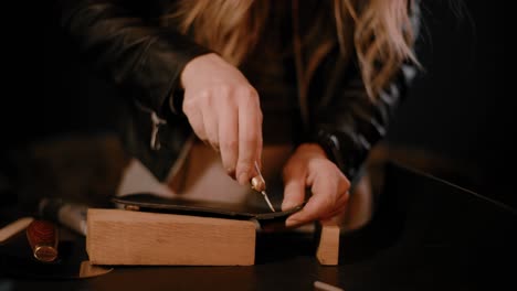 Manos-De-Mujer-Usando-Una-Herramienta-De-Lezna-En-Cuero-Negro-En-El-Taller,-Perforando-Agujeros,-Configuración-Oscura,-Alto-Contraste,-Clasificación-De-Color