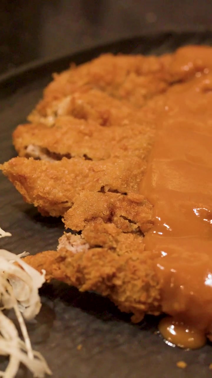 Macro shot of crispy breaded pork cutlet topped with thick gravy on black plate.