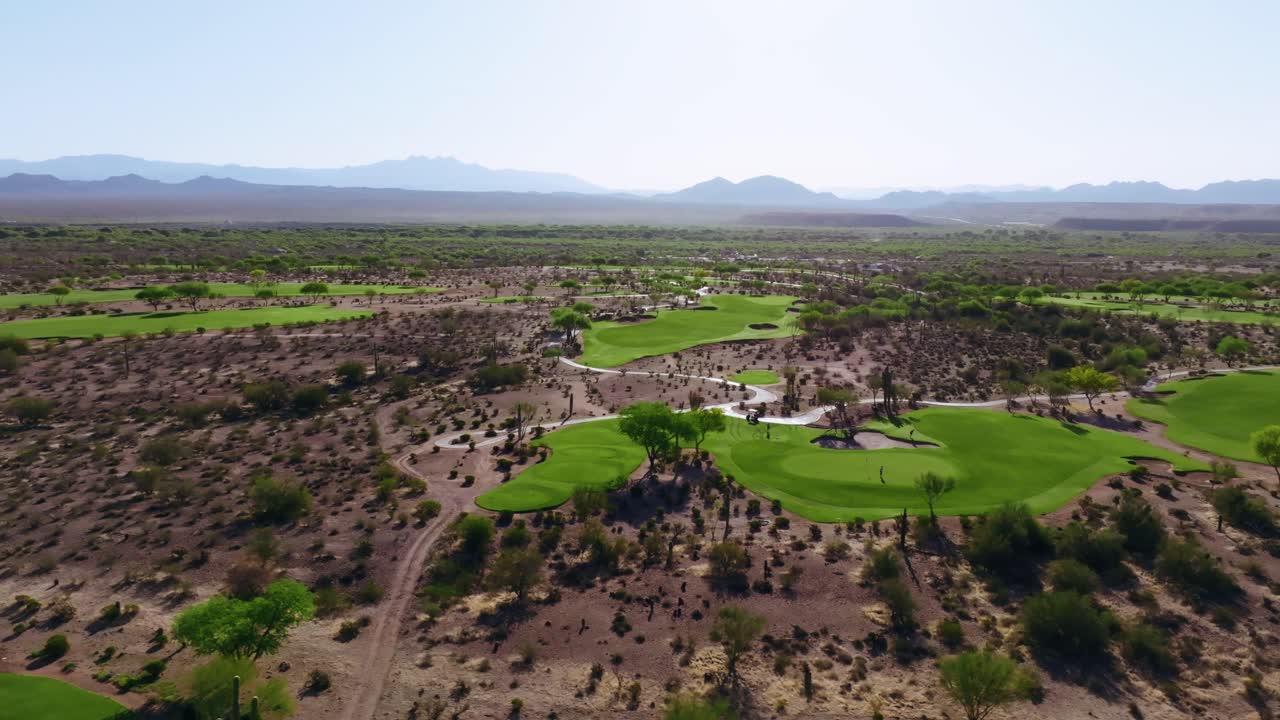 Wide aerial view of multiple desert golf holes woven through cactus-covered terrain with distant mountains