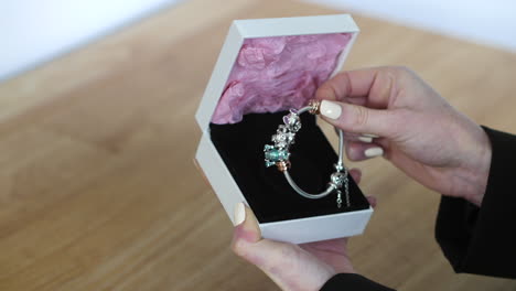 una mujer recibiendo una caja de regalos con un brazalete de encanto adentro