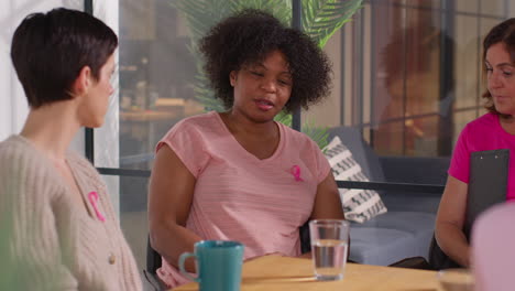 group of women wearing pink breast cancer awareness ribbons meeting and talking at therapy support group for cancer treatment patients 7