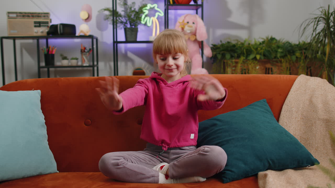 Child kid girl smiling friendly at camera waving hands gesturing hello hi greeting at home on couch
