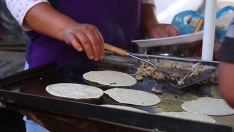 mujer cocinando carne y volteando tortillas para hacer tacos en un puesto ambulante