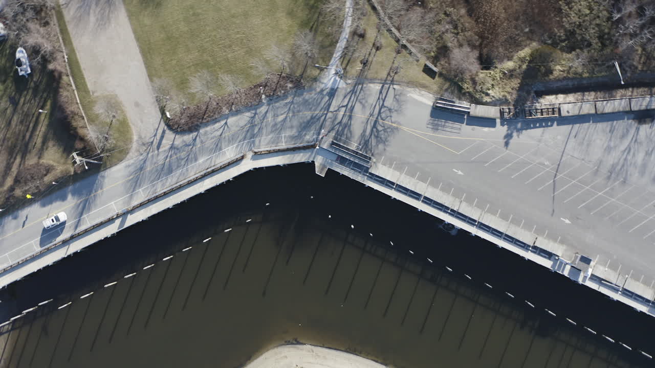 The camera looks down and gives a birds eye view of Rock Harbor (Orleans, Ma) marina at low tide. There is a small exposed shoreline due to the low tide. Docked boats can be seen along the marina path