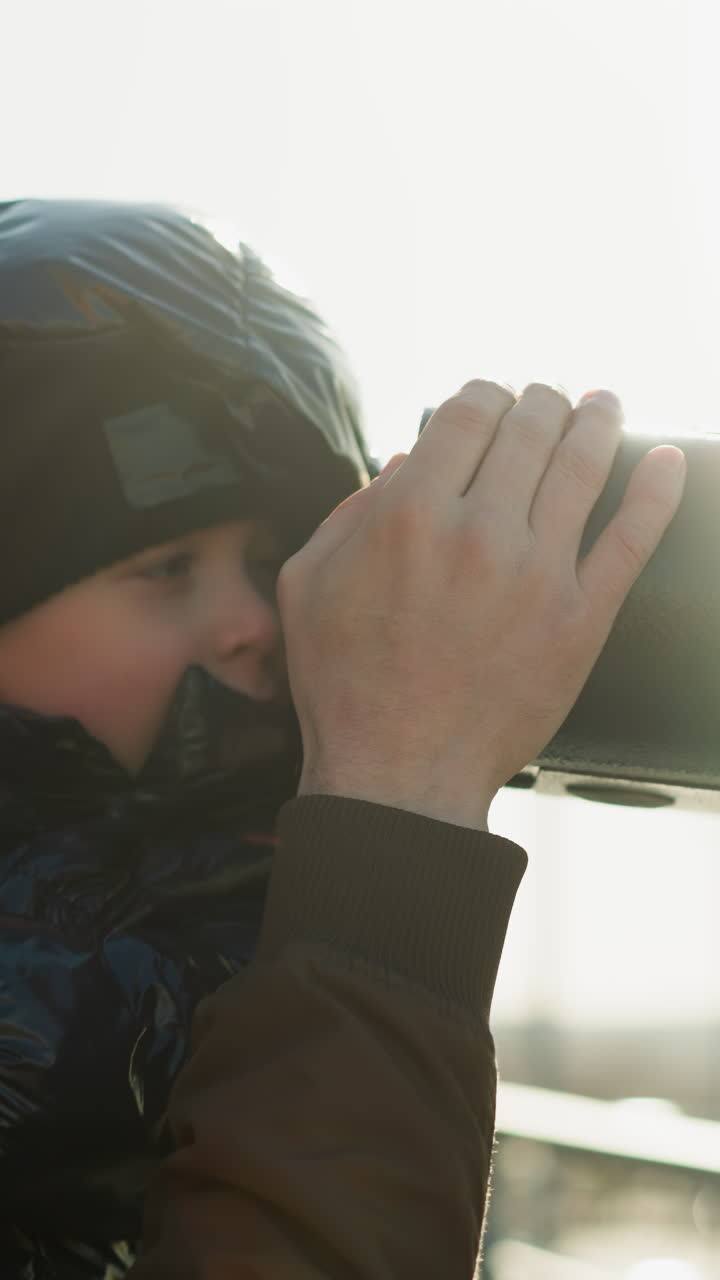아버지가 망원경 앞에 아들을 들고, 호기심으로 망원경을 들여다보면서 그를 안내합니다.아버지는 미소 짓고, 한 시야를 보장하기 위해 망원을 지지합니다.