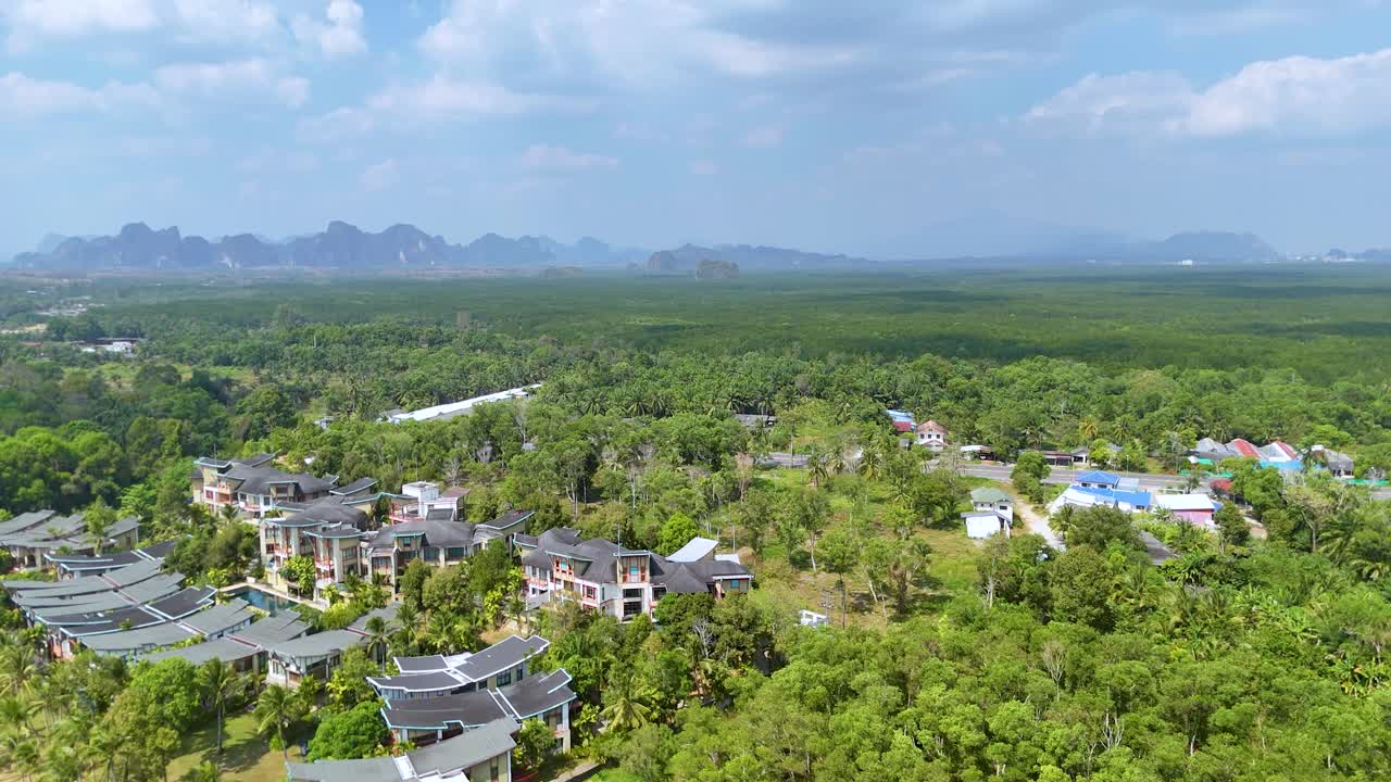 Drone footage captures luxury villas surrounded by dense tropical jungle and distant karst mountains