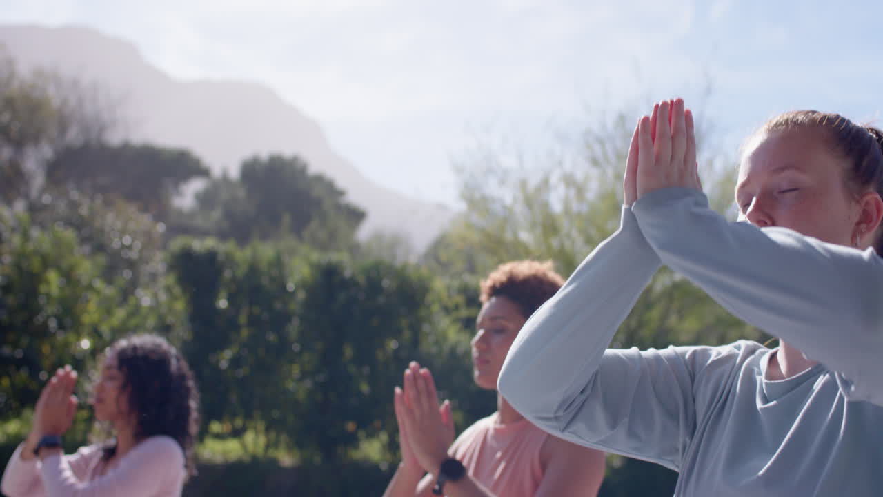 Practicing yoga outdoors, diverse female friends meditating with hands in prayer position, copy spac