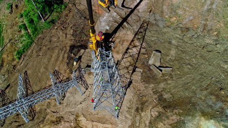 toma aérea de arriba hacia abajo del trabajador en la construcción de una nueva torre de transmisión en el campo durante el día soleado - toma de seguimiento