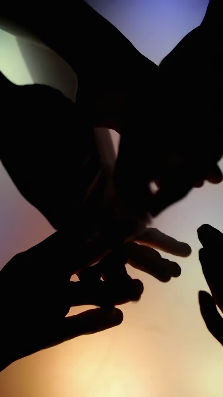 Silhouetted hands in unity from a low angle, with a gradient background, video concept