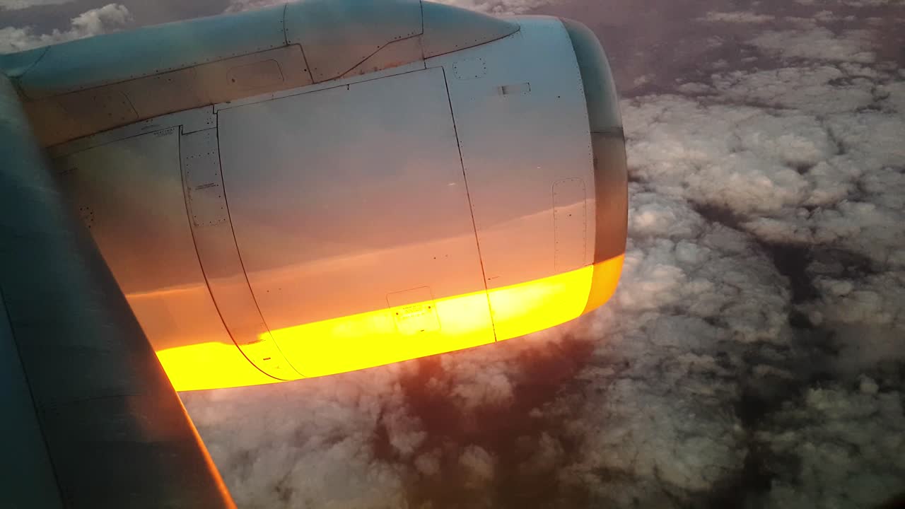 Sunset shining on plane engine and light white clouds below 4k