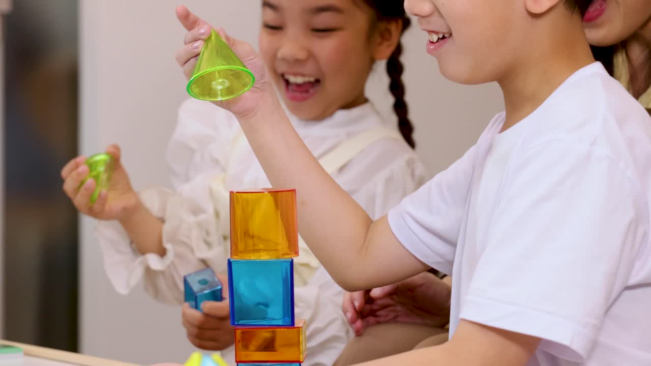 Dua anak menumpuk balok warna-warni bersama, tertawa dan belajar di lingkungan kelas yang cerah.