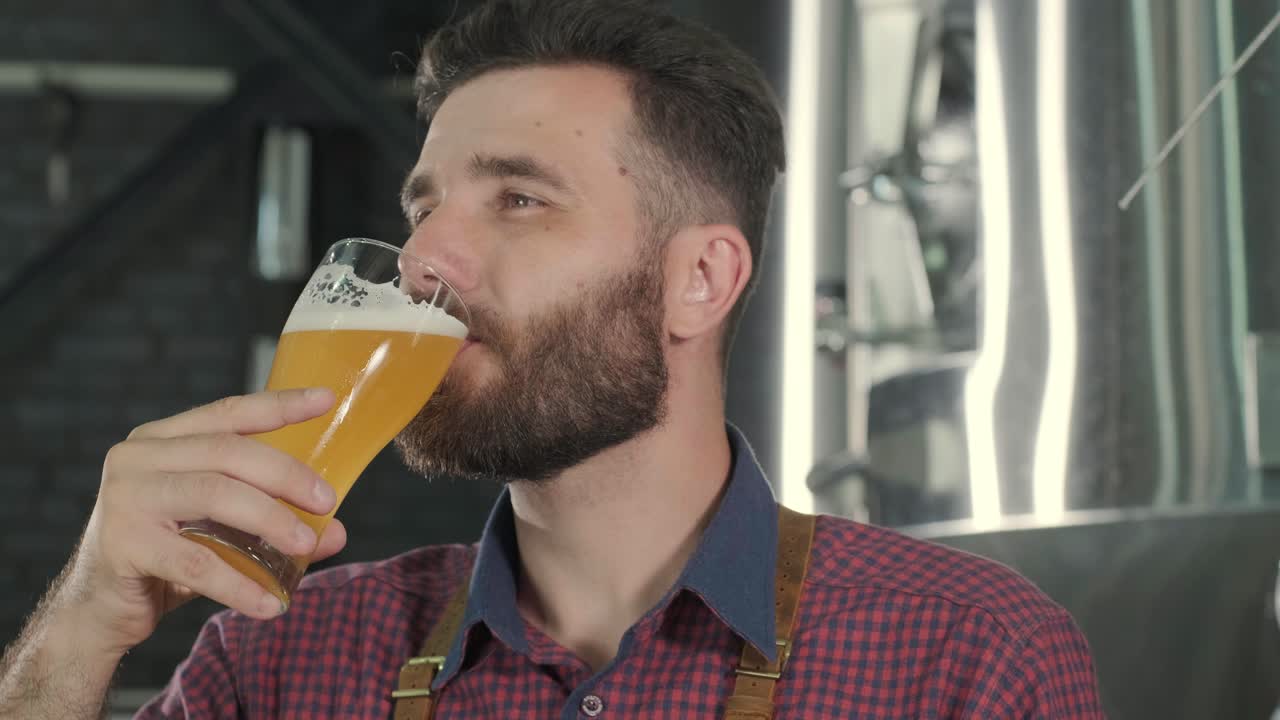 un joven cervecero con un delantal de cuero está probando cerveza en una cervecería moderna