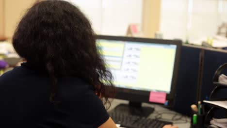 Over-shoulder-view-of-dark-hair-woman-using-computer-in-office-workplace