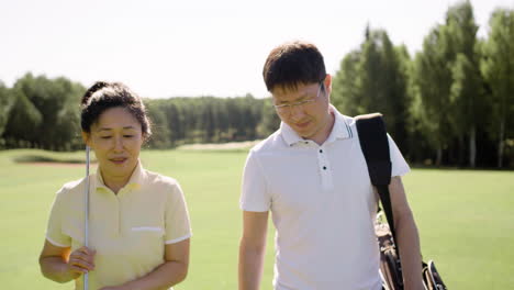 Man-in-glasses-and-woman-with-golf-club-talking-and-walking-on-field