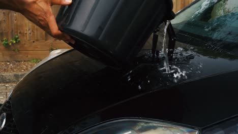 person pouring a bucket of water over the bonnet on their car