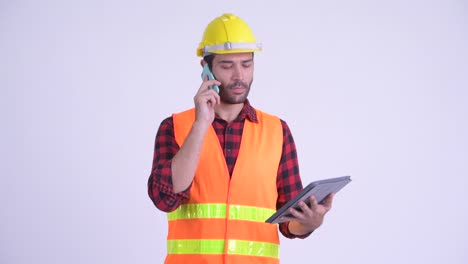 hombre persa barbudo y guapo trabajador de la construcción con teléfono y tableta digital
