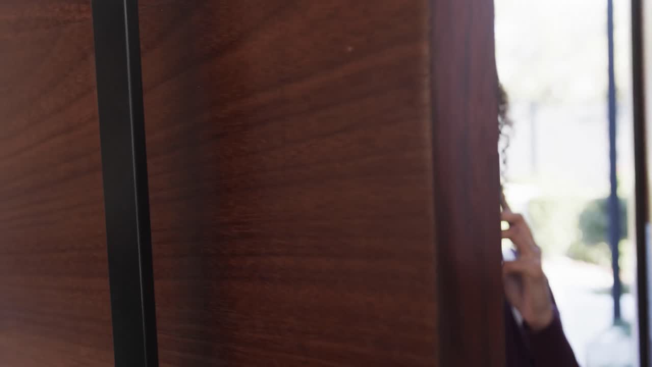 feliz pareja de lesbianas biraciales llegando a casa y hablando en el teléfono inteligente, en cámara lenta