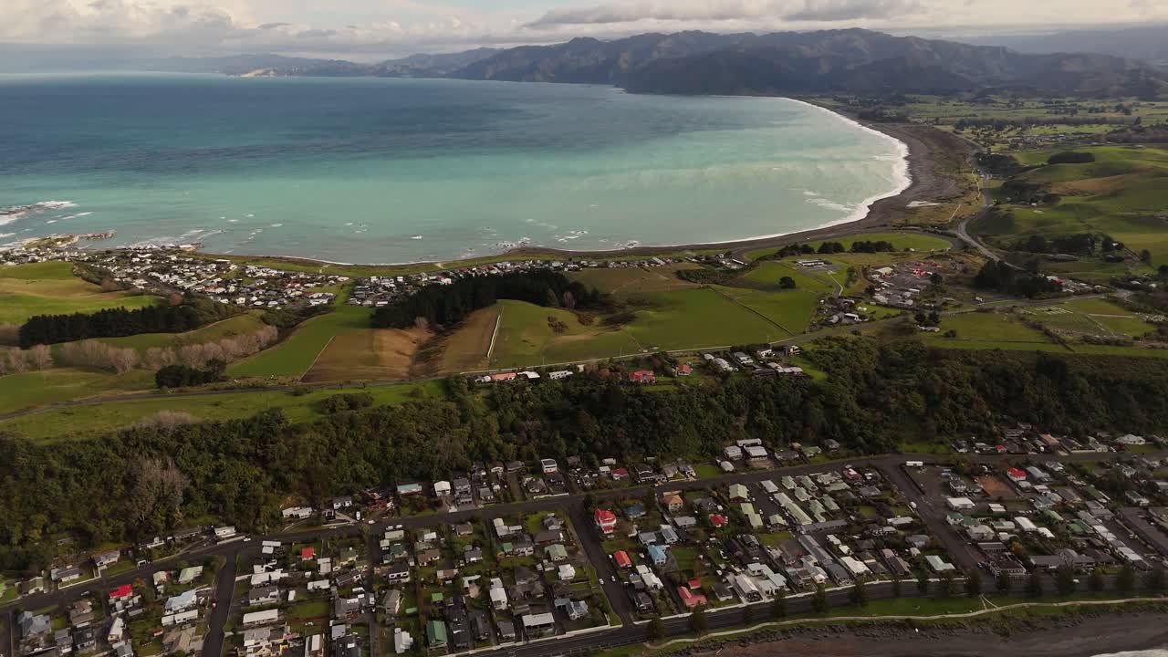 Aerial top down of kaikoura area with houses and homes in south New Zealand. Panning shot. Turquoise bay wave along beach. Villas on hills