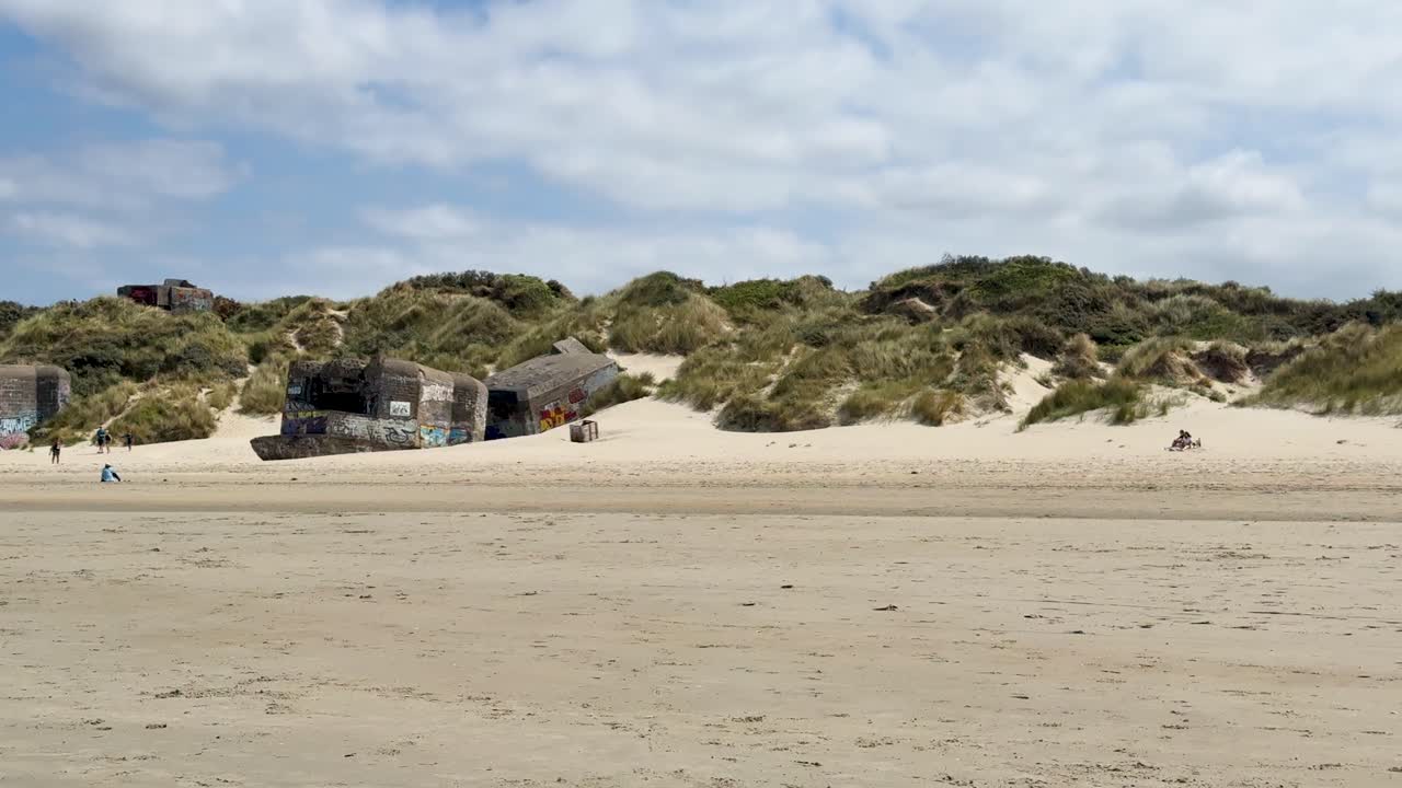 A slow camera pan reveals historical concrete World War II bunkers on a sunny beach