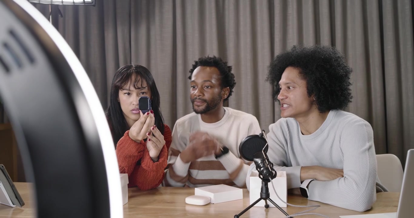 Diverse creators recording in studio with phone in ring light, unboxing wrist device for review