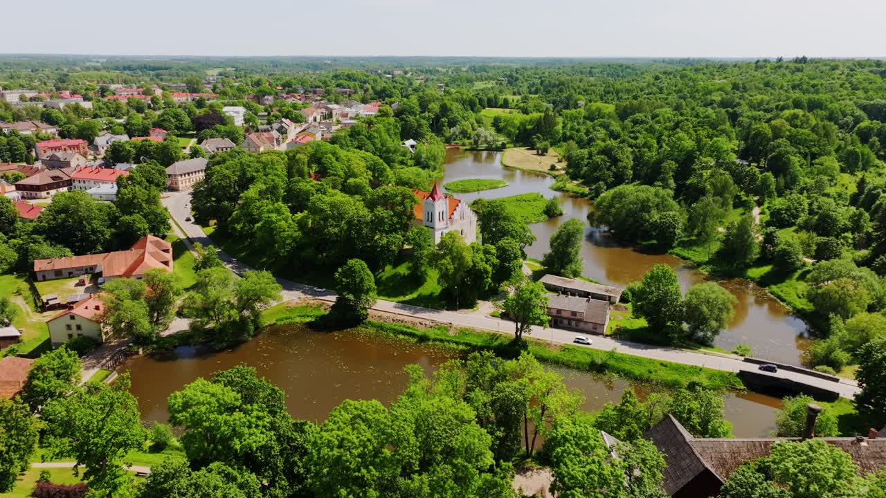 Cinematic aerial highlights Aizpute’s main road and St John’s Lutheran Church