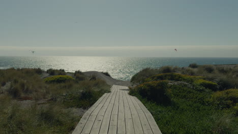 empty boardwalk going off into beach with calm ocean in background with silhouette of kite surfers