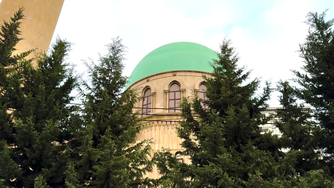 A mosque with a distinct green dome peeks through tall trees in Baku. Baku, Azerbaijan