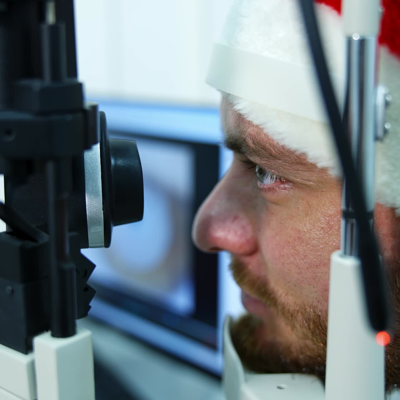 Patient treating eyes in clinic. Profile view of a man's face in Christmas cap looking into special device in ophthalmology center. Close-up