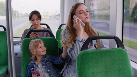 young family woman with kid girl sitting in public bus transport, mother talking on mobile phone