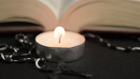 Rosary-beads-and-single-tea-light-with-open-bible-in-background