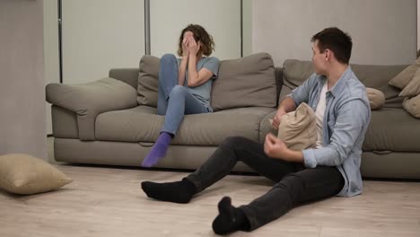 chica caucásica joven molesta sentirse ofendida por su novio o marido mientras está sentado en el suelo. mujer arrojando almohadas sobre él y luego comenzó a gritar. gran pelea en la relación matrimonial