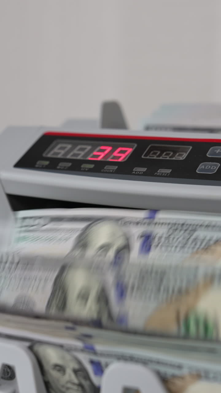 Man puts a wad of USD dollars into cash counting equipment. Banknotes with Benjamin Franklin portrait turning in the machine. Close up. Vertical video