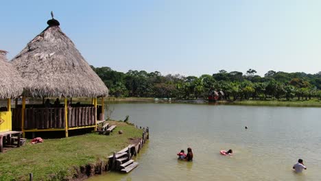 4k daytime aerial drone video with people swimming into the warm waters and near a house on the laguna de los milagros, tingo maria, the peruvian amazon