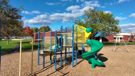 Bunter-Spielplatz-Mit-Rutschen-Und-Schaukeln,-Sonniger-Tag,-Schule-Im-Hintergrund