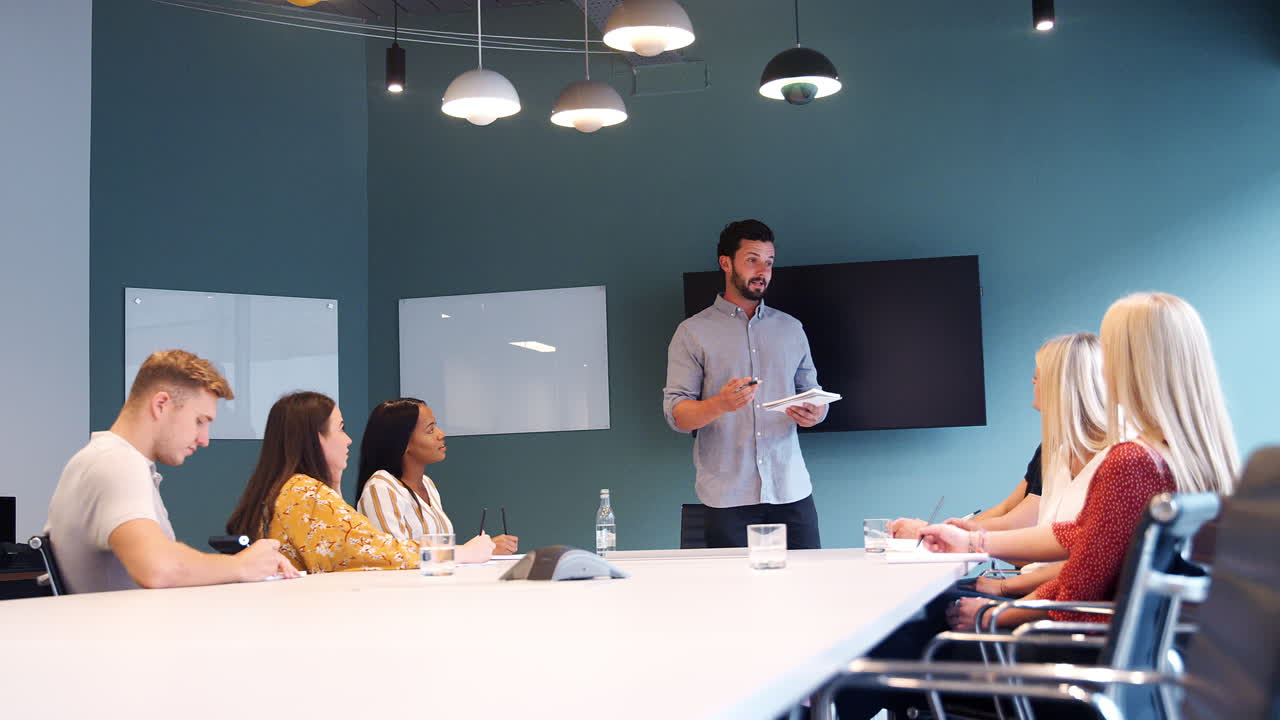 empresario dirigiéndose a un grupo de candidatos reunidos alrededor de una mesa en el día de evaluación de reclutamiento de graduados