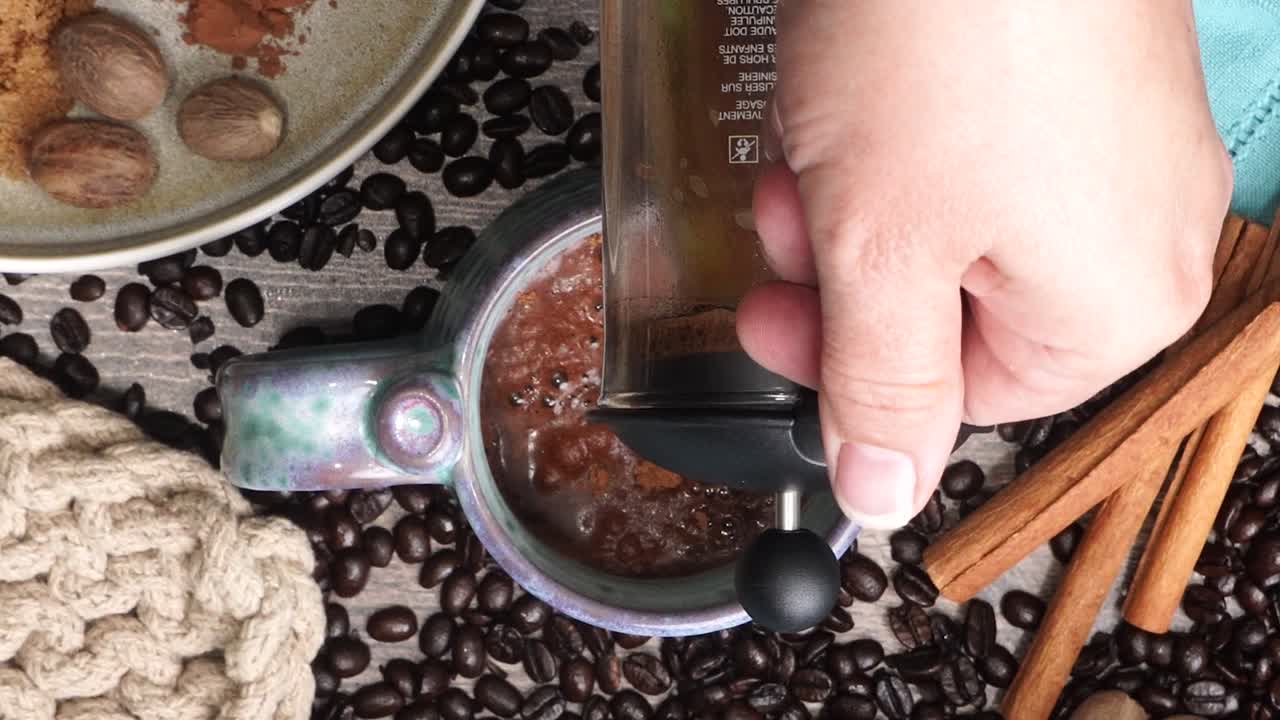 Cup or mug of coffee in a blue ceramic cup with whipped cream and a dash of nutmeg or cinnamon. Coffee beans surrounding a cozy cup of coffee in a blue mug.