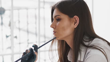 artista con cabello largo mano sucia sostiene pincel cerca de la ventana