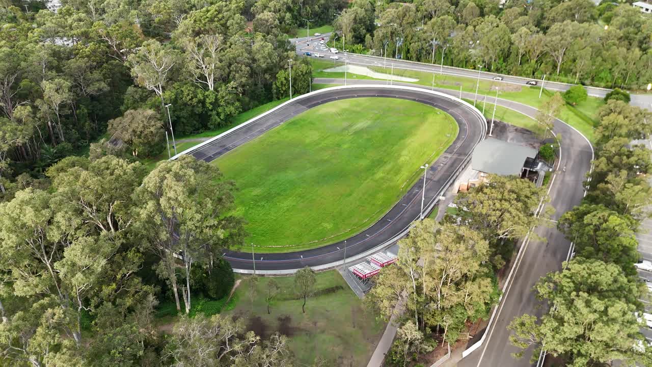 Drone footage captures the lush, green velodrome surrounded by trees, showcasing the serene environment and smooth track layout
