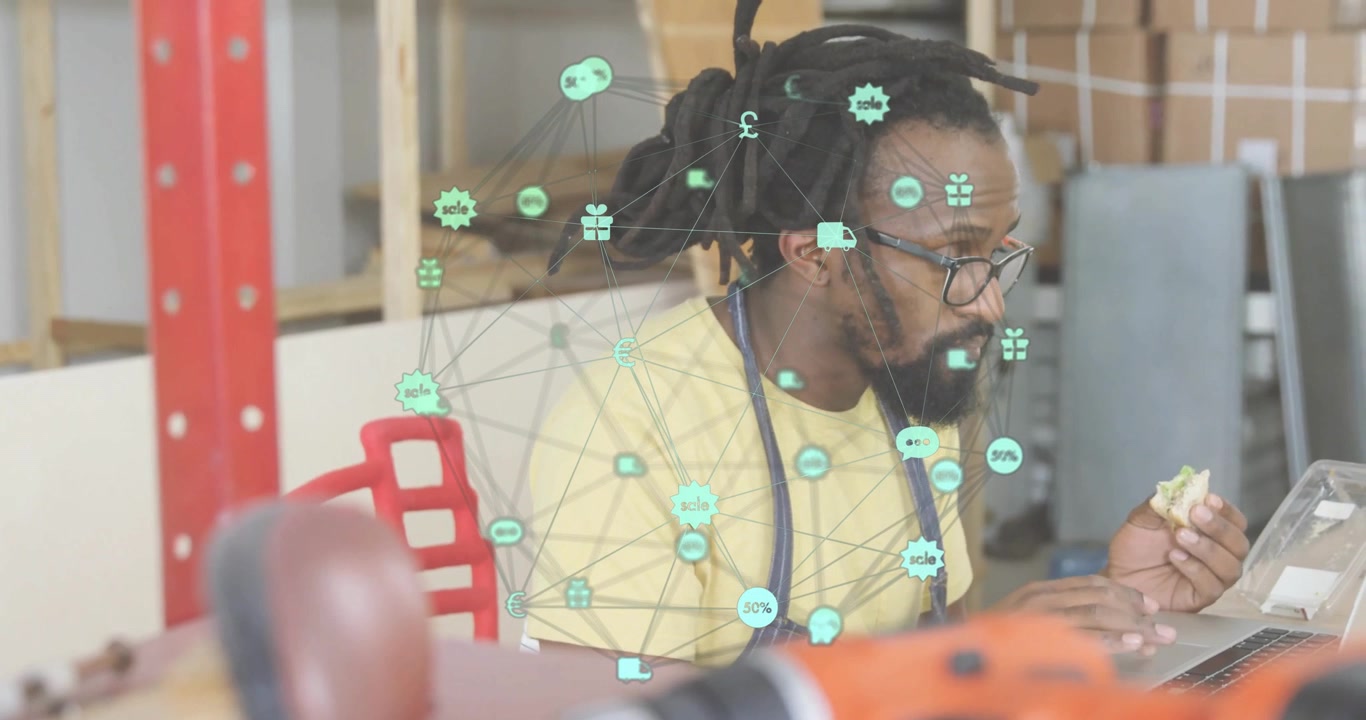 Man sitting at workbench eating snack while typing on laptop, showing neon-green e-commerce icons