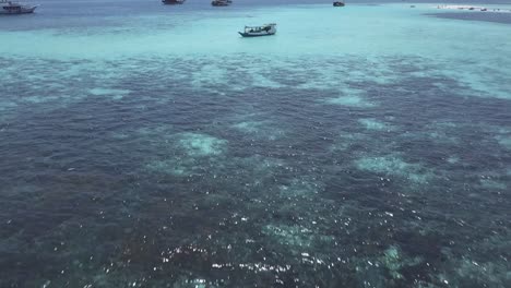Aerial-drone-shot-over-some-boats-sailing-through-the-sea-in-an-idyllic-turquoise-seascape-with-an-island-in-the-background