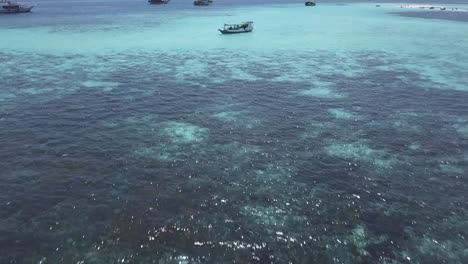 aerial drone shot over some boats sailing through the sea in an idyllic turquoise seascape with an island in the background