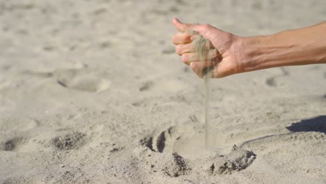 off-center of a hand scooping up sand and pouring on a sunny beach