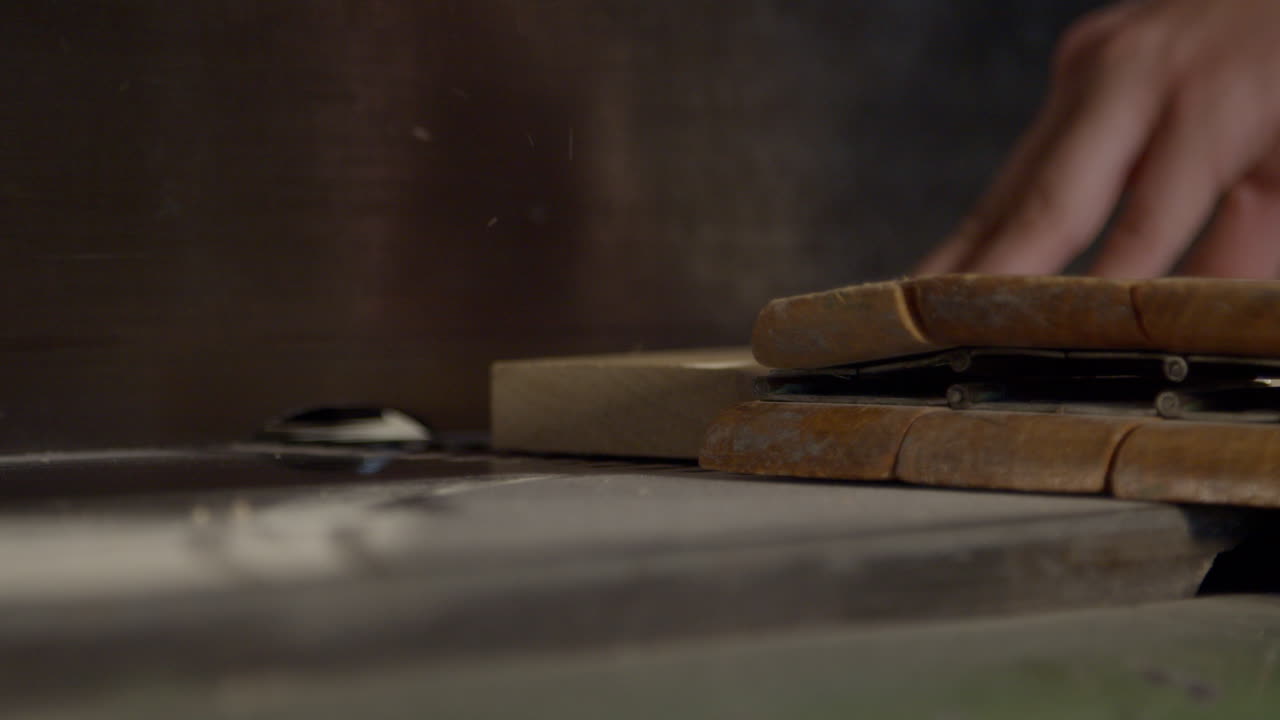 High quality video of a hand guiding a wooden board across a saw in warm cinematic light. Slow motion captures dust, grain and precise woodworking in a calm workshop atmosphere