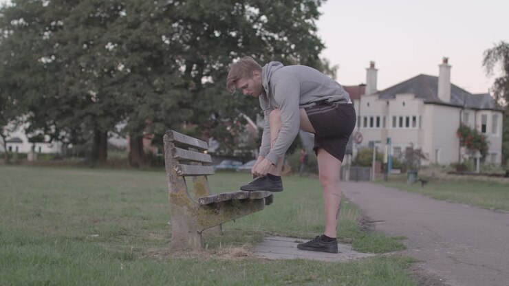 Young Attractive Man Tying His Shoes on a Bench Before He Sets of For a Run, In Slow Motion - Ungraded