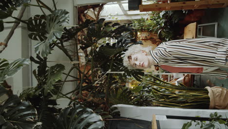 young woman looking at plant and posing for camera in flower shop