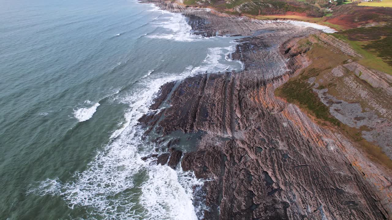 AERIAL: Fly towards along textured rocky coastline with crashing waves, Port Eynon Gower, 4k Drone