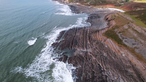aéreo: volar hacia una costa rocosa texturizada con olas rompientes, port eynon gower, drone 4k