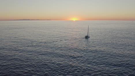 Sailing-yacht-floating-across-the-ocean-at-sunset-towards-the-horizon