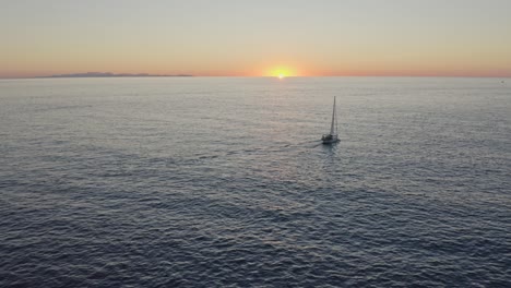 sailing yacht floating across the ocean at sunset towards the horizon